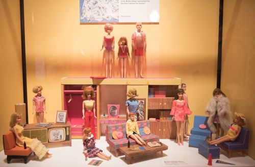 A display of vintage dolls in a colorful living room setting, showcasing various outfits and furniture pieces.