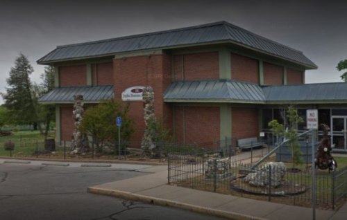 A brick building with a metal roof, surrounded by trees and a small fence, featuring a sign that reads "Spoke Museum."