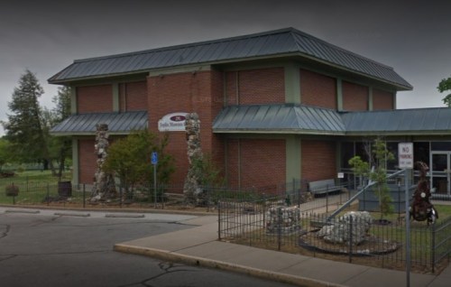 A brick building with a metal roof, featuring stone sculptures and a "No Parking" sign outside.