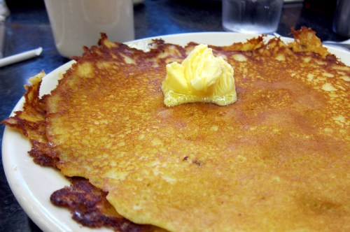 A golden-brown pancake topped with a pat of butter on a white plate.