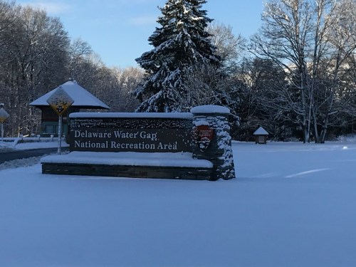 Sign for Delaware Water Gap National Recreation Area covered in snow, surrounded by trees and a winter landscape.