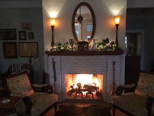Cozy living room with a glowing fireplace, two armchairs, and decorative lights on the mantel.