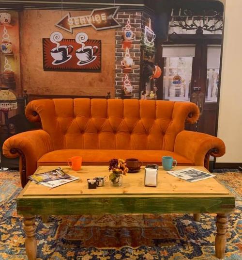 A cozy orange sofa with a wooden coffee table, surrounded by decorative items and a café-style backdrop.