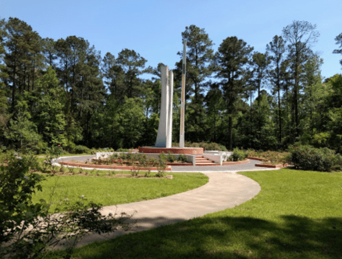 A memorial with tall white pillars surrounded by greenery and a pathway, set in a peaceful park.