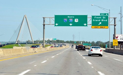 Highway scene with green exit signs for I-29, I-35, and Grand Blvd, featuring a cable-stayed bridge in the background.