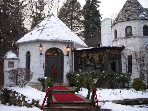 A charming snow-covered house with a circular entrance, adorned with holiday decorations and a red carpet pathway.