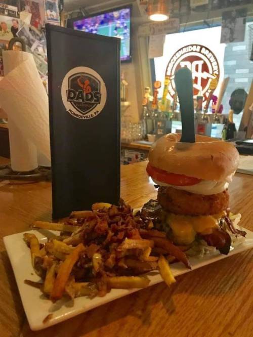 A towering burger made with a donut bun, stacked with toppings, served with a side of fries and bacon bits.