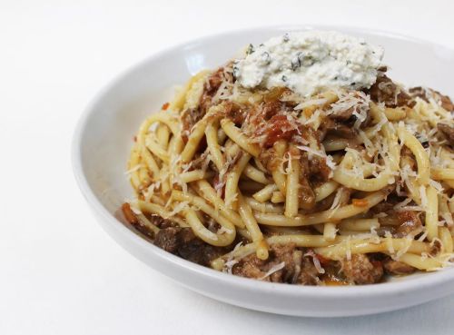 A bowl of spaghetti topped with meat sauce, ricotta cheese, and grated Parmesan.