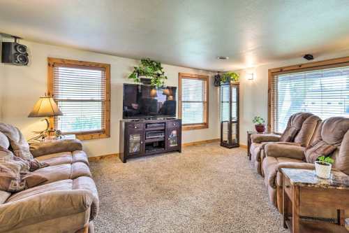 Cozy living room with plush seating, a TV, and natural light from windows, featuring plants and warm decor.