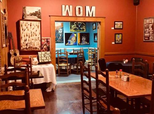 Cozy restaurant interior with wooden tables, chairs, and colorful artwork on the walls, featuring a blue room in the background.