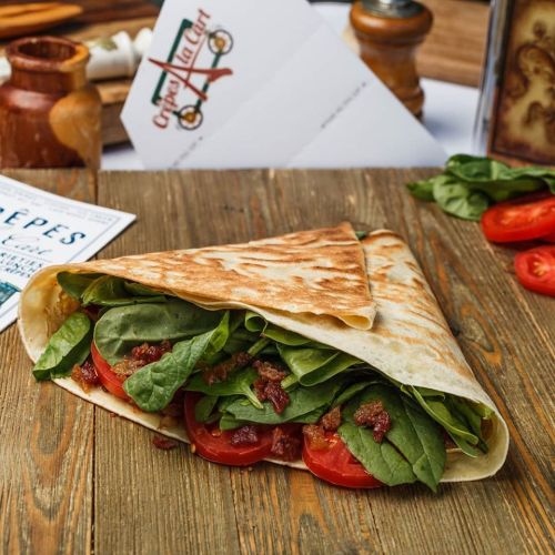 A delicious wrap filled with fresh spinach, tomatoes, and bacon, resting on a wooden table.