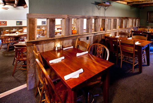 Cozy restaurant interior with wooden tables, chairs, and rustic decor, featuring a partition and warm lighting.