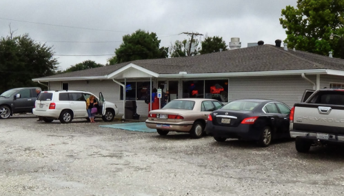 A small restaurant with a gravel parking lot, featuring several parked cars and a person getting out of a white van.