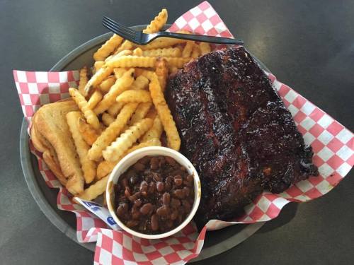 A plate of BBQ ribs with crinkle-cut fries, baked beans, and two slices of bread, served in a basket with a checkered liner.