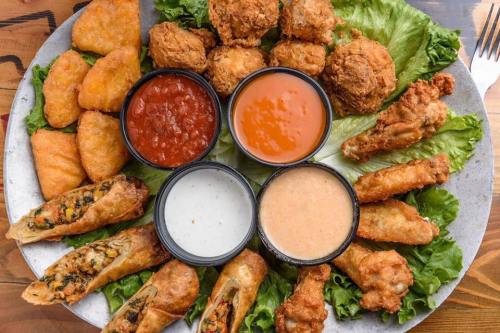 A platter of assorted fried foods, including wings, nuggets, and egg rolls, served with various dipping sauces on lettuce.