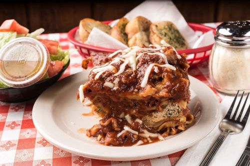 A hearty serving of lasagna topped with marinara sauce and cheese, accompanied by a side salad and breadsticks.