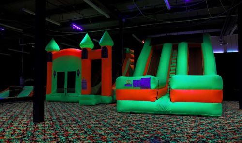 Brightly colored inflatable bounce house and slide in a dark indoor space with neon lighting.
