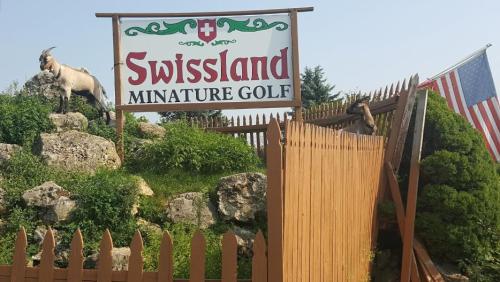Sign for "Swissland Miniature Golf" with goats on rocks and an American flag nearby.