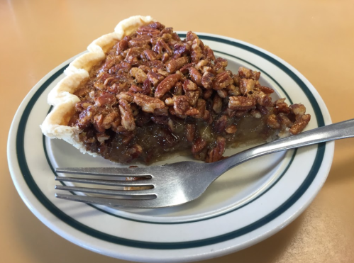 A slice of pecan pie on a plate with a fork, featuring a golden crust and a crunchy pecan topping.