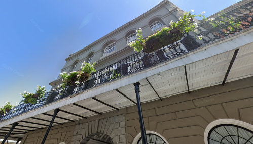 A low-angle view of a historic building with a balcony adorned with potted plants against a clear blue sky.