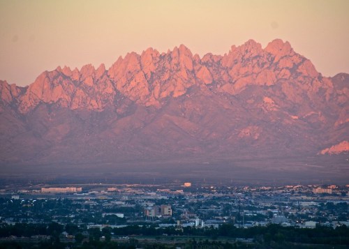 Sunset over rugged mountains with a cityscape in the foreground, showcasing a blend of natural and urban landscapes.