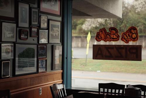 Interior of a pizza restaurant with framed photos on the wall and a view of the street through a window.