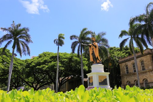 A statue surrounded by palm trees and lush greenery under a clear blue sky.