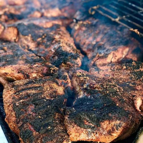 Close-up of grilled meat with a smoky, charred surface, sizzling on a barbecue grill.