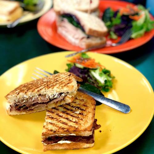 A grilled sandwich with layers of meat and cheese on a yellow plate, accompanied by a small salad.