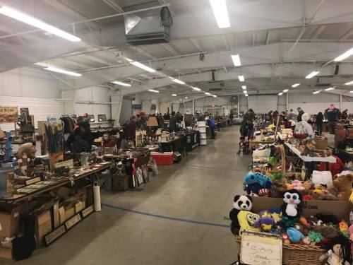 A bustling indoor market with various vendor tables displaying crafts, antiques, and plush toys.