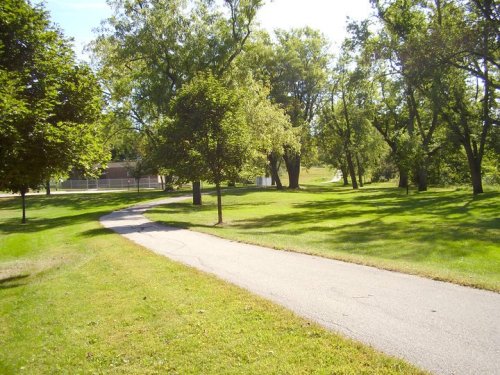 A winding path through a lush green park, lined with trees under a clear blue sky.