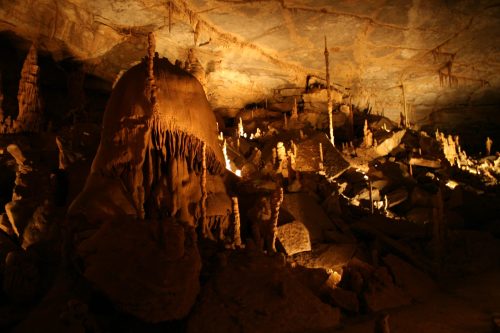 A dimly lit cave interior featuring stalactites, stalagmites, and rocky formations illuminated by soft lighting.
