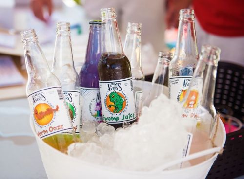 A bucket filled with ice and various colorful soda bottles, each labeled with unique names like "Swamp Juice" and "Worm Ooze."