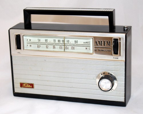 A vintage transistor radio with a black and silver design, featuring AM and FM tuning dials and a handle on top.