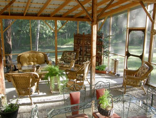Cozy screened porch with wicker furniture, plants, and a serene view of trees outside.