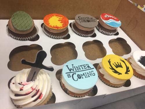 A box of themed cupcakes featuring designs from "Game of Thrones," including houses and iconic symbols.