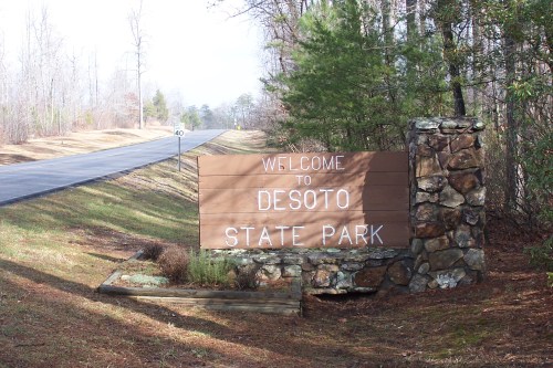 Welcome sign for Desoto State Park, surrounded by trees, with a road visible in the background.