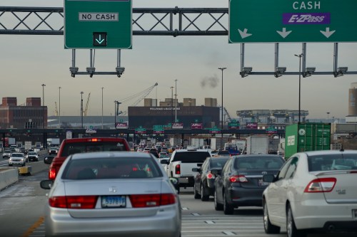 Traffic congestion on a highway with signs indicating cash and electronic toll options in the background.