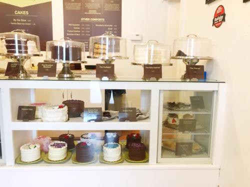 Display case filled with various cakes, including layered and frosted options, in a cozy bakery setting.