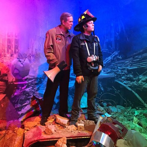 A firefighter stands on rubble, with a figure in a jacket holding a megaphone, set against a colorful background.