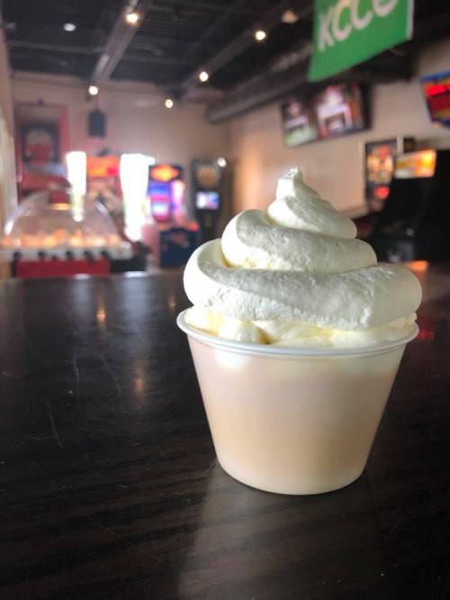A soft-serve ice cream in a cup, with an arcade in the background and soft lighting.