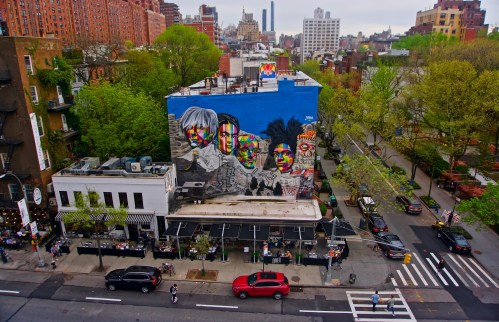 Colorful mural on a building in an urban setting, featuring stylized portraits against a blue background.
