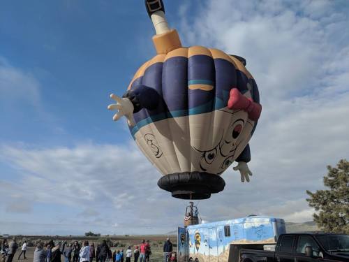 A colorful hot air balloon shaped like a cartoon character rises above a crowd at an outdoor event.