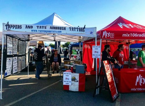 A vibrant outdoor market scene featuring tattoo booths and promotional tents under a clear blue sky.