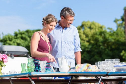 A couple smiles while browsing items at an outdoor market, surrounded by colorful glassware and greenery.