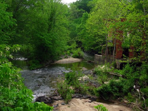 A serene river flows through lush greenery, with a brick structure partially hidden among the trees.