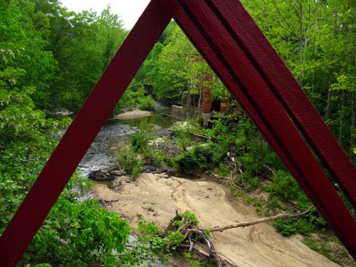 View of a lush green landscape with a creek, framed by a red bridge structure.