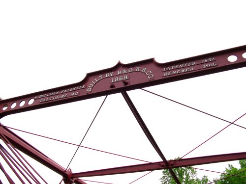 Historic iron bridge structure with a red frame, featuring the inscription "Built by B&O R.R. Co. Patented 1852, Renewed 1866."