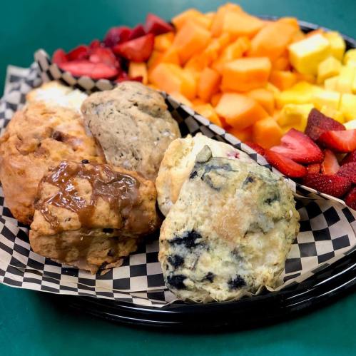A platter of assorted scones and fresh fruit, including strawberries, cantaloupe, and mixed tropical fruits.
