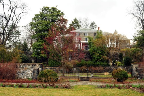 A historic mansion surrounded by lush greenery and a stone wall, set against a cloudy sky.